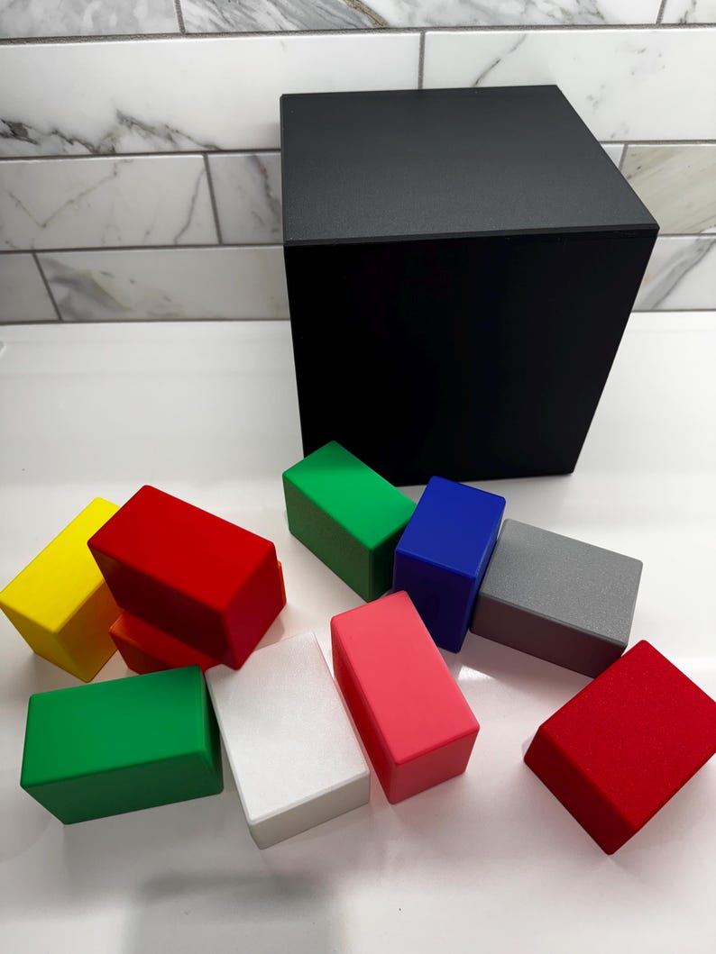 May include: A set of ten colorful wooden blocks in various colors, including red, green, yellow, blue, pink, white, and gray. The blocks are arranged on a white surface in front of a black cube.