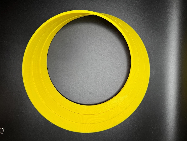 May include: A yellow plastic ring with three concentric circles. The ring is on a black background.
