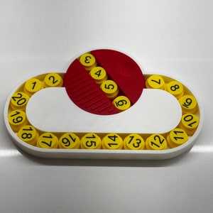 May include: A white plastic toy with a red and white circular piece in the center. The toy has a ring of yellow circles with numbers 1 through 20 around the outside.