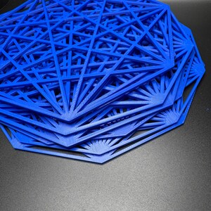May include: A stack of blue, geometric, 3D printed coasters. The coasters are made of a thin, plastic-like material and have a starburst design.