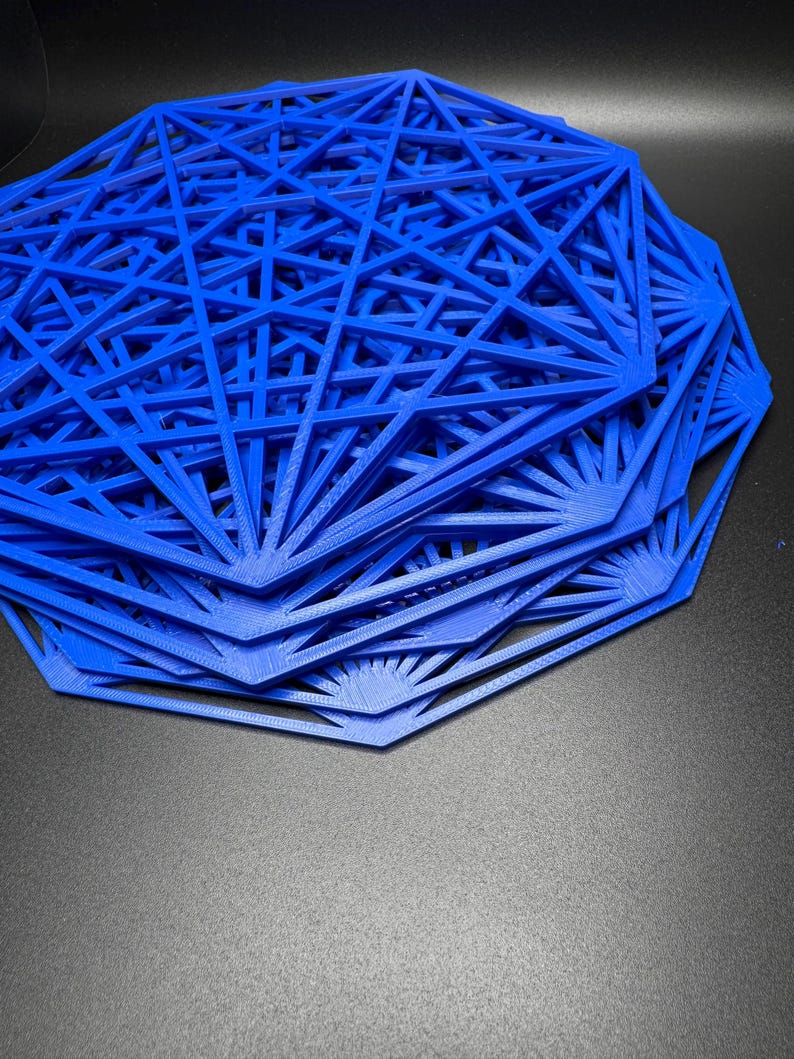 May include: A stack of blue, geometric, 3D printed coasters. The coasters are made of a thin, plastic-like material and have a starburst design.