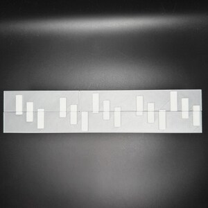 May include: A white plastic ruler with black markings. The ruler is divided into sections with different lengths. The ruler is a useful tool for measuring and drawing.