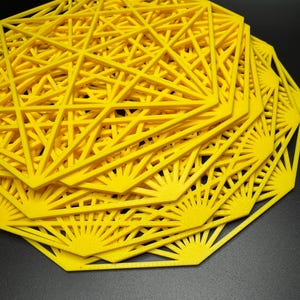 May include: A stack of yellow geometric coasters with a starburst design. The coasters are made of a lightweight material and have a delicate, intricate pattern.