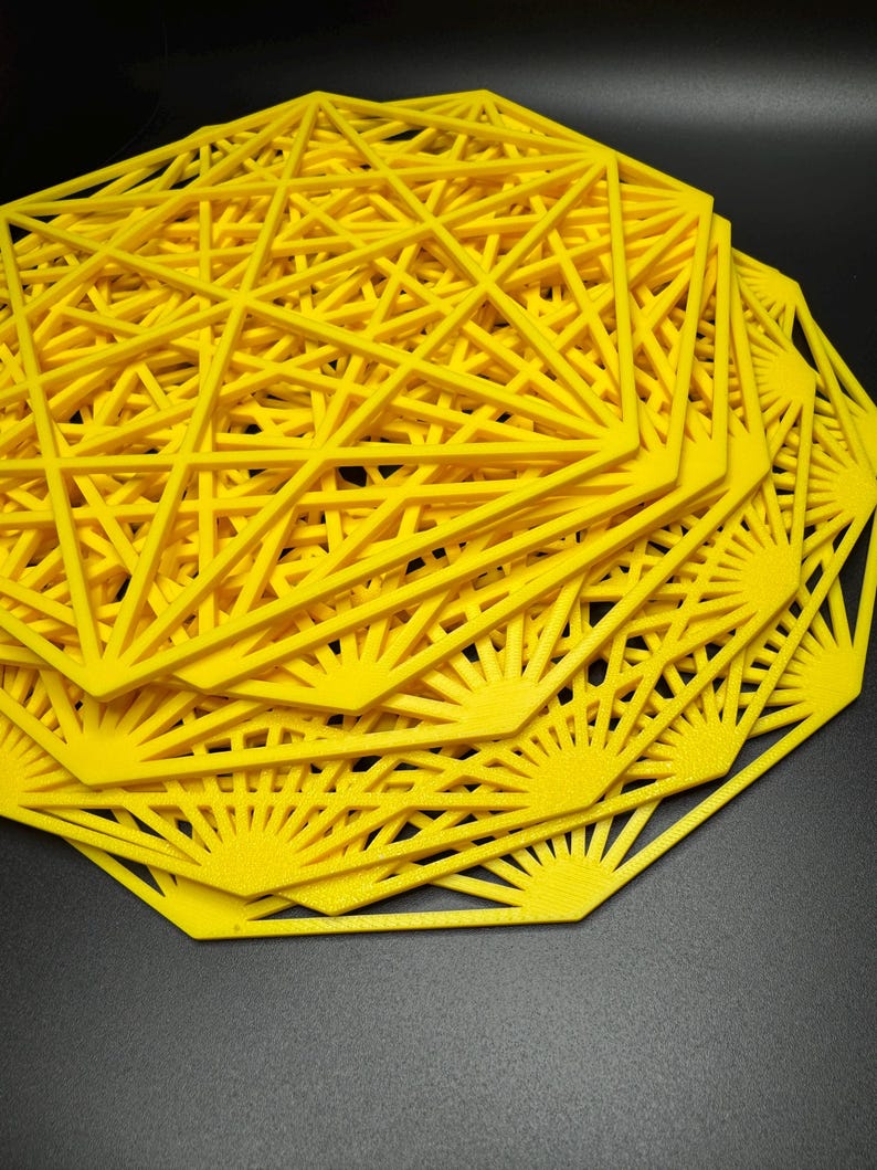 May include: A stack of yellow geometric coasters with a starburst design. The coasters are made of a lightweight material and have a delicate, intricate pattern.