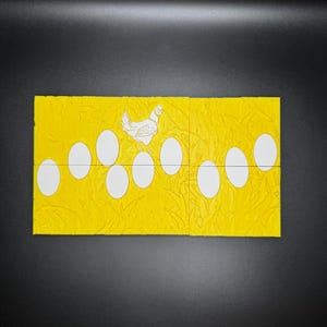 May include: A yellow cardstock with a white chicken and 10 white eggs. The chicken is standing on top of the eggs. The cardstock has a textured pattern.