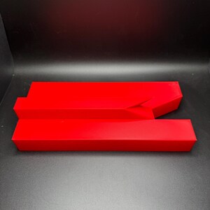 May include: A red plastic object with a unique shape, resembling a split or broken rectangle. The object is made of a smooth, glossy plastic and has a bright red colour.