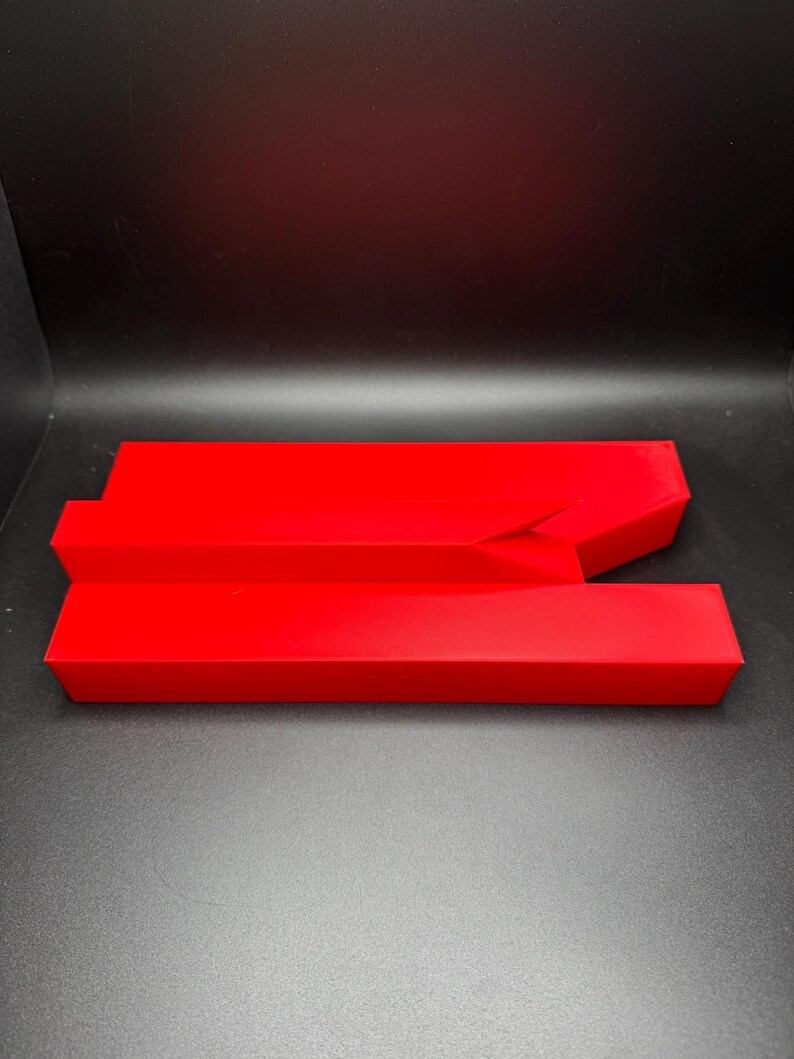 May include: A red plastic object with a unique shape, resembling a split or broken rectangle. The object is made of a smooth, glossy plastic and has a bright red colour.