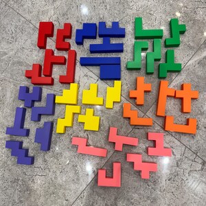 May include: A set of colourful Tetris-like puzzle pieces in red, blue, green, yellow, and orange. The pieces are made of plastic and are arranged in a circular pattern on a grey tiled floor.