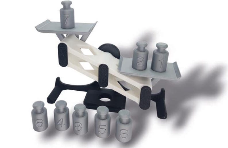 May include: A white and black seesaw toy with gray plastic weights numbered 1 through 7. The seesaw is balanced with weights 2 and 1 on one side and weight 7 on the other side. There are six additional weights on the ground, numbered 6, 4, 3, 5, 5, and 3.