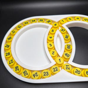 May include: A white plastic organiser tray featuring a figure-eight shape with two circular compartments. The tray is lined with forty small, yellow, cylindrical pegs, each marked with a black number ranging sequentially from one to forty.