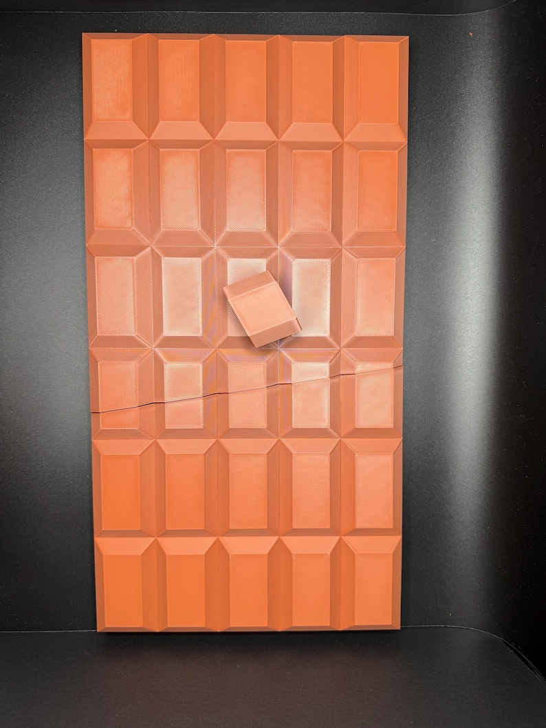 May include: A large, rectangular chocolate bar with a broken piece missing. The bar is made of individual squares and is a deep orange colour.