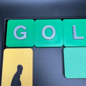May include: Green tiles with the letters G, O, and L in white on them. The tiles are on a black surface.