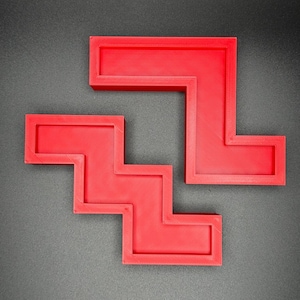 May include: Two red plastic puzzle pieces shaped like a staircase and an L. The pieces fit together to form a larger shape.