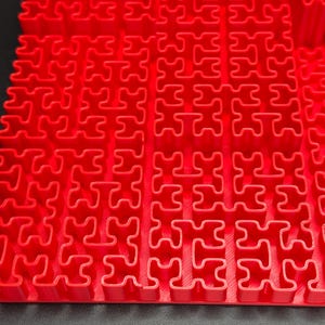 May include: A red plastic puzzle mat with interlocking pieces in the shape of a puzzle. The mat is made of a flexible material and is designed to be used on the floor.