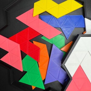 May include: A colorful set of geometric puzzle pieces in a black tray. The pieces are made of plastic and are shaped like triangles. The colors of the pieces are red, orange, yellow, green, blue, and purple.