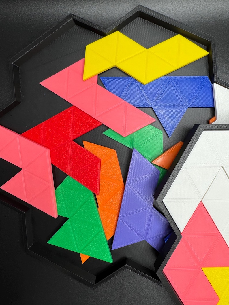 May include: A colorful set of geometric puzzle pieces in a black tray. The pieces are made of plastic and are shaped like triangles. The colors of the pieces are red, orange, yellow, green, blue, and purple.