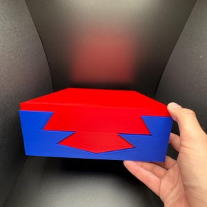 May include: A red and blue wooden puzzle box with a geometric design. The box is closed and has a lid that is slightly ajar.