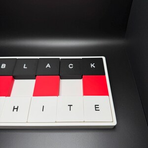 May include: A rectangular puzzle with alternating black, red, and white tiles. The black tiles spell out "BLACK" and the white tiles spell out "WHITE". The puzzle is set against a black background.