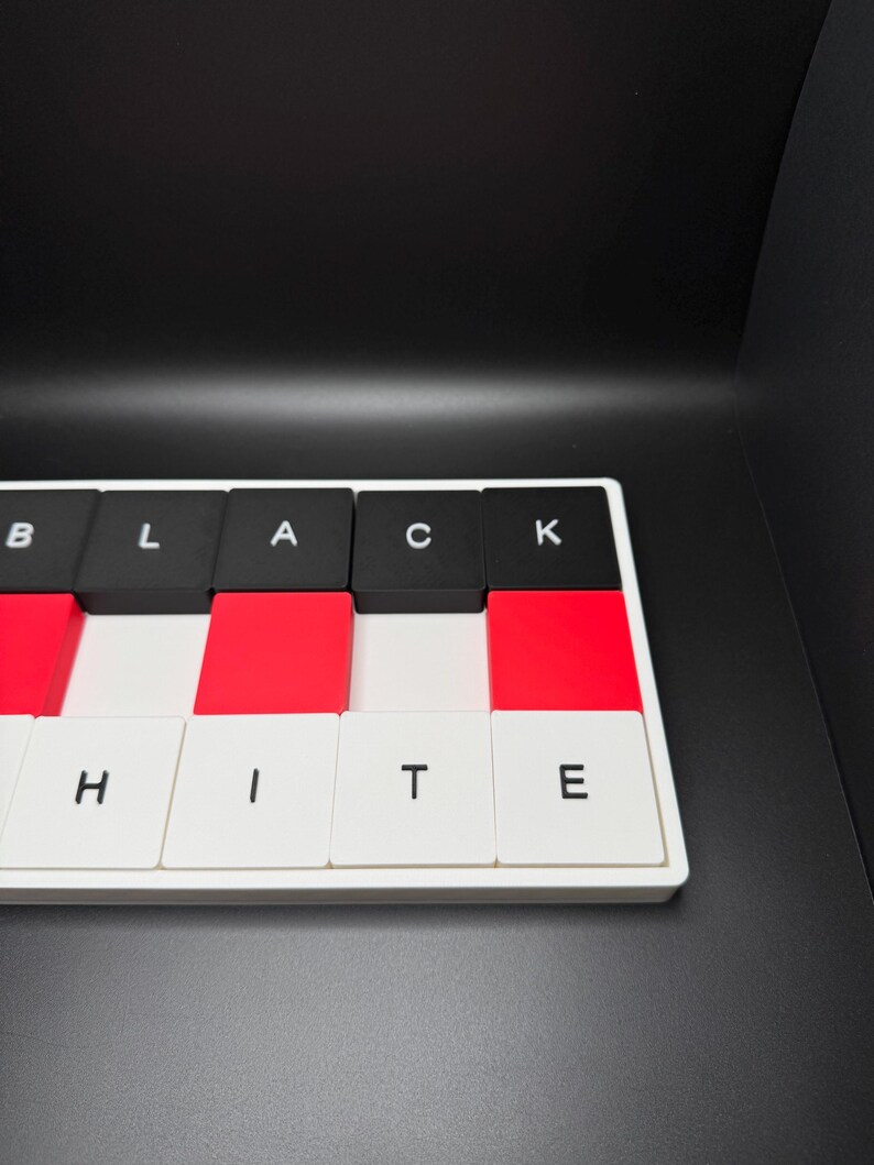 May include: A rectangular puzzle with alternating black, red, and white tiles. The black tiles spell out "BLACK" and the white tiles spell out "WHITE". The puzzle is set against a black background.