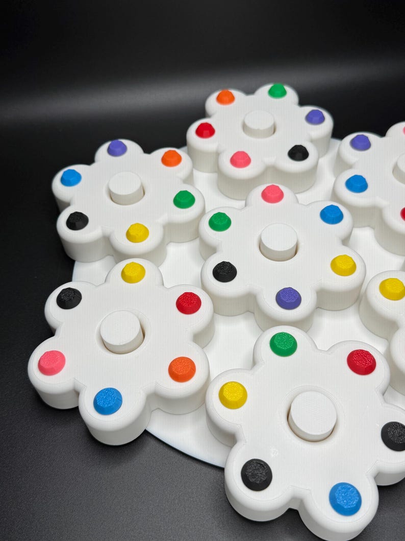 May include: White, flower-shaped toys with colorful dots. Each flower has a central circular piece and six petals, each with a different colored dot. The colors include red, orange, yellow, green, blue, purple, pink, and black.