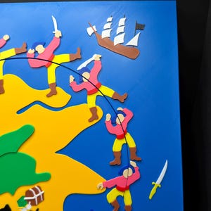 May include: A colorful, 3D-printed pirate-themed artwork. The piece features a blue background with a yellow and green landmass. Figures in pink shirts and yellow pants are depicted with weapons, a treasure chest, and a ship.