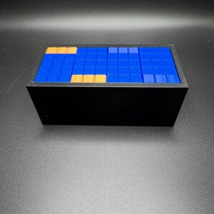 May include: A black rectangular box with a blue and gold tiled top. The tiles are arranged in a pattern.