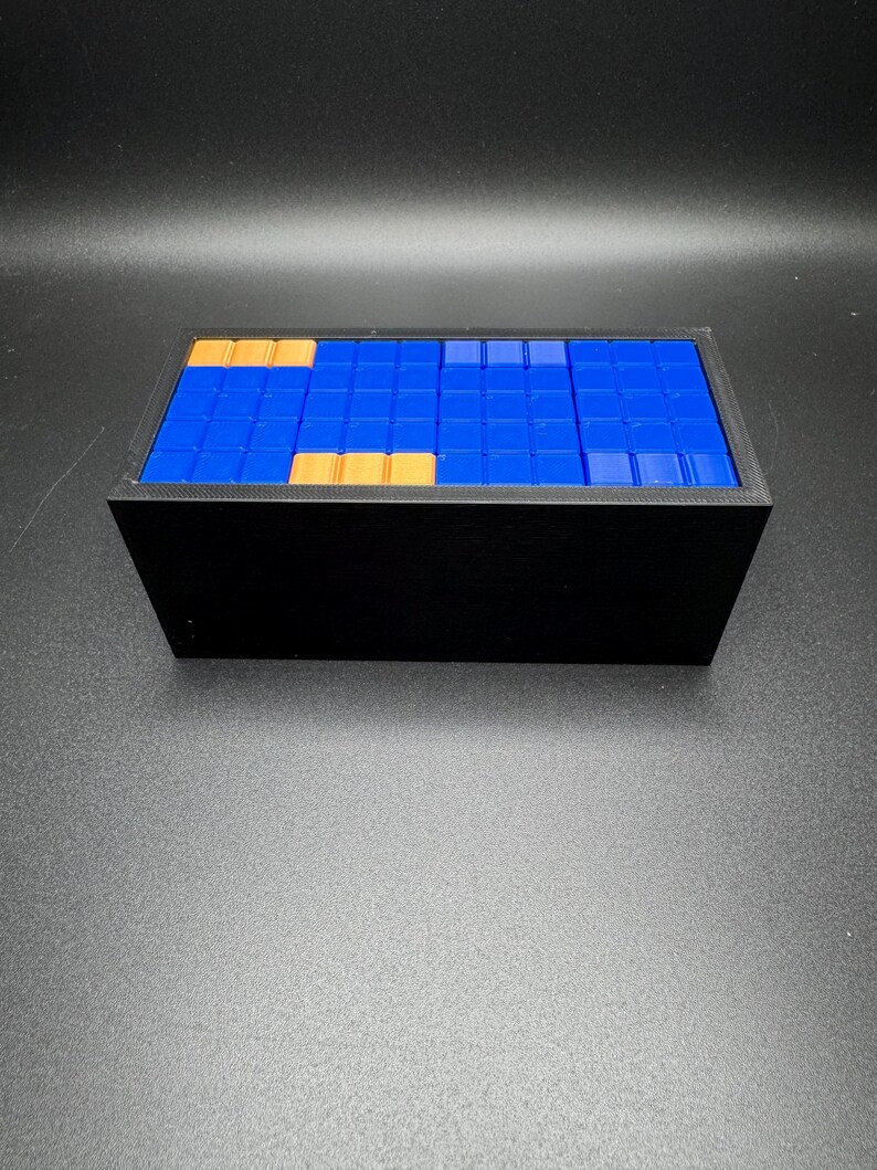 May include: A black rectangular box with a blue and gold tiled top. The tiles are arranged in a pattern.