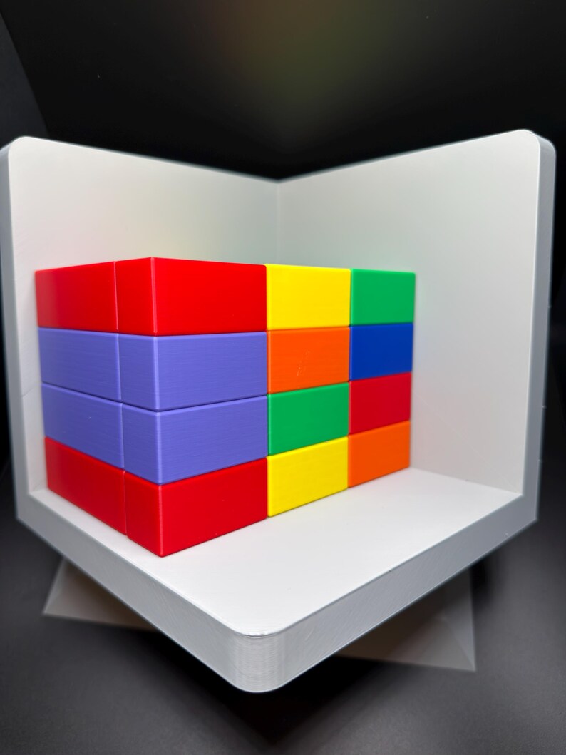 May include: A rectangular block structure composed of multiple smaller, solid-colored bricks in red, purple, yellow, green, blue, and orange. The bricks are arranged in a grid pattern and are positioned inside a white, L-shaped corner display stand.