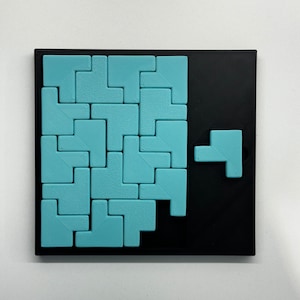May include: A blue and black puzzle game with a variety of blue Tetris-like pieces on a black board. One blue piece is missing from the board and is shown separately.