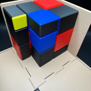 May include: A 3D puzzle with a wooden base and nine colourful blocks. The blocks are red, blue, black, and yellow. The puzzle is assembled in a tower shape.