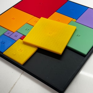 May include: A colorful puzzle with different sized squares, each with a number printed on it. The numbers include 8, 11, 17, 19, 23, 25, 29, 35, 37, 50, and 12. The puzzle is made of plastic and is set on a black frame.