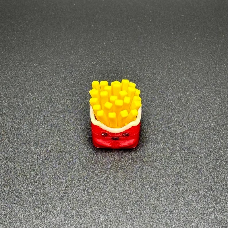 May include: A small, red and white cartoon french fry container with a smiling face. The container is filled with yellow french fries.
