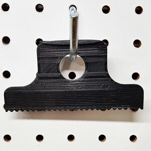 May include: Black plastic scraper tool with a serrated edge and a hole for hanging. The tool is hanging on a pegboard.