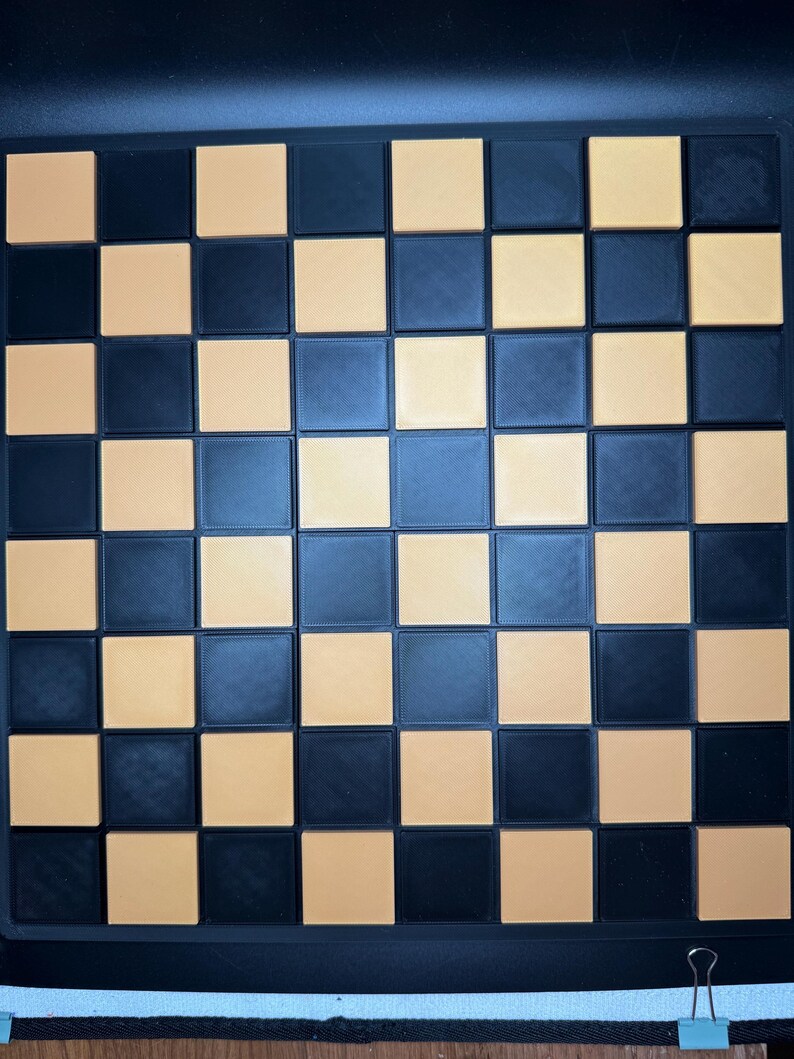 K&ouml;nnte beinhalten: Ein schwarz-beiges Schachbrett mit einem Rastermuster. Die Quadrate wechseln sich zwischen Schwarz und Beige ab. Das Brett besteht aus einem strapazierf&auml;higen Material und ist zum Schachspielen konzipiert.