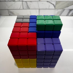 May include: A colorful cube made of small blocks. The cube is made of red, yellow, blue, green, and gray blocks. The blocks are arranged in a pattern.