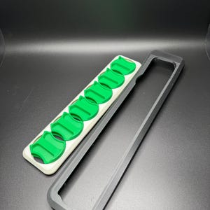 May include: A white and black plastic case with a row of six green plastic inserts. The case is open and the inserts are visible.