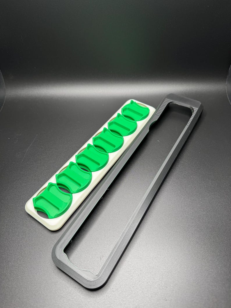 May include: A white and black plastic case with a row of six green plastic inserts. The case is open and the inserts are visible.