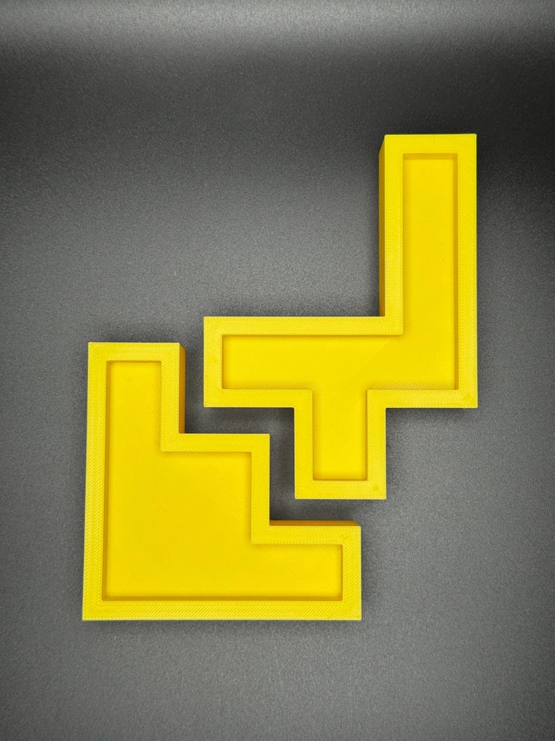 May include: Two yellow plastic puzzle pieces shaped like an L and a T, joined together to form a larger shape.