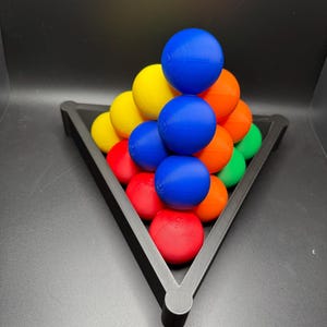 Peut inclure: Un plateau triangulaire noir contient une pyramide de boules color&eacute;es. Les boules sont dispos&eacute;es en forme de pyramide, la boule du haut &eacute;tant bleue, la couche suivante &eacute;tant jaune, puis orange, puis rouge et enfin verte.