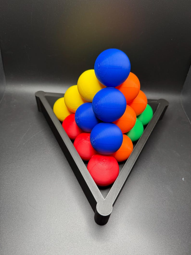 Peut inclure: Un plateau triangulaire noir contient une pyramide de boules color&eacute;es. Les boules sont dispos&eacute;es en forme de pyramide, la boule du haut &eacute;tant bleue, la couche suivante &eacute;tant jaune, puis orange, puis rouge et enfin verte.