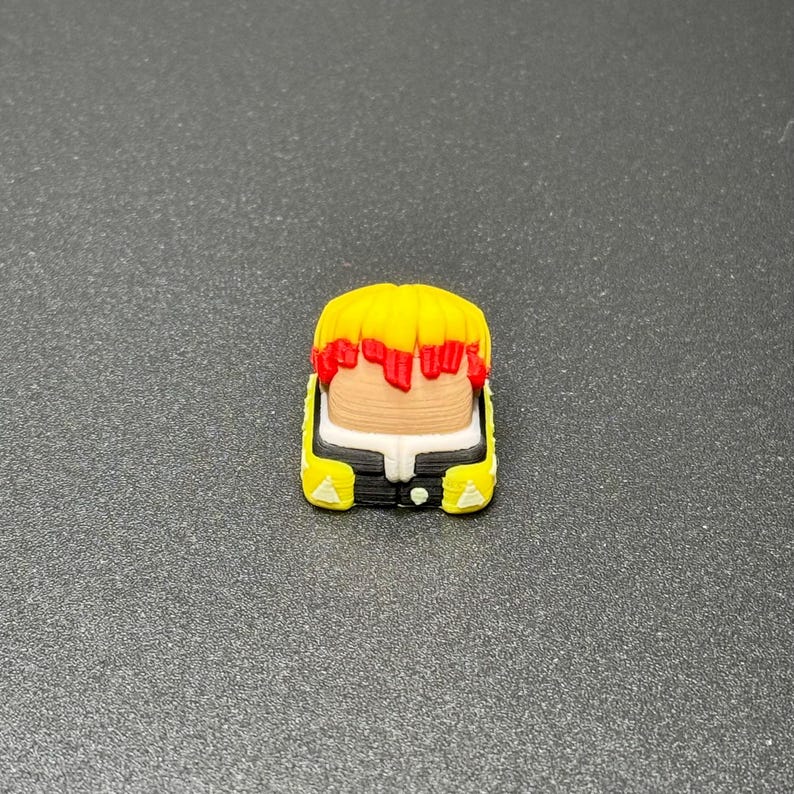 May include: A yellow and red keycap with a black and white design. The keycap features a stylized face with a yellow head and red hair.