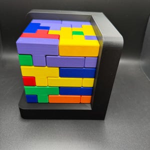 May include: A colorful wooden block puzzle with a black frame. The blocks are arranged in a pattern, with different colors including purple, yellow, blue, green, red, and orange.