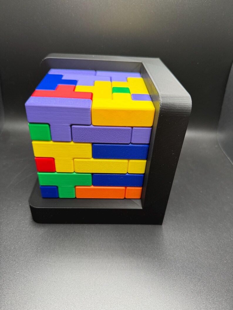 May include: A colorful wooden block puzzle with a black frame. The blocks are arranged in a pattern, with different colors including purple, yellow, blue, green, red, and orange.
