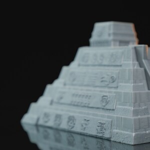 May include: A gray model of a Mayan pyramid with intricate carvings and details. The pyramid is made of a smooth, textured material and has a slightly weathered appearance.