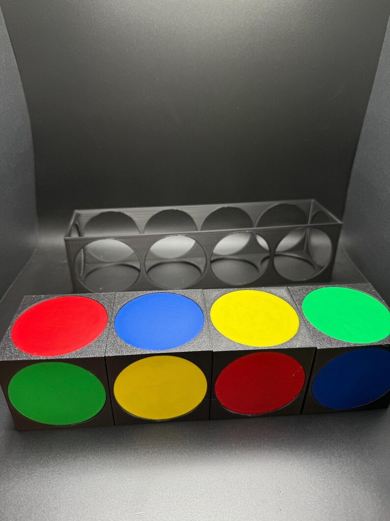 May include: A black storage unit with eight circular openings, and a matching set of eight black cubes. Each cube has a coloured, oval-shaped insert in red, blue, yellow, and green.