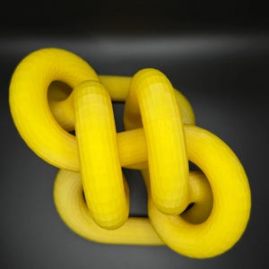 May include: A yellow plastic sculpture of a knot, with a smooth, glossy finish.