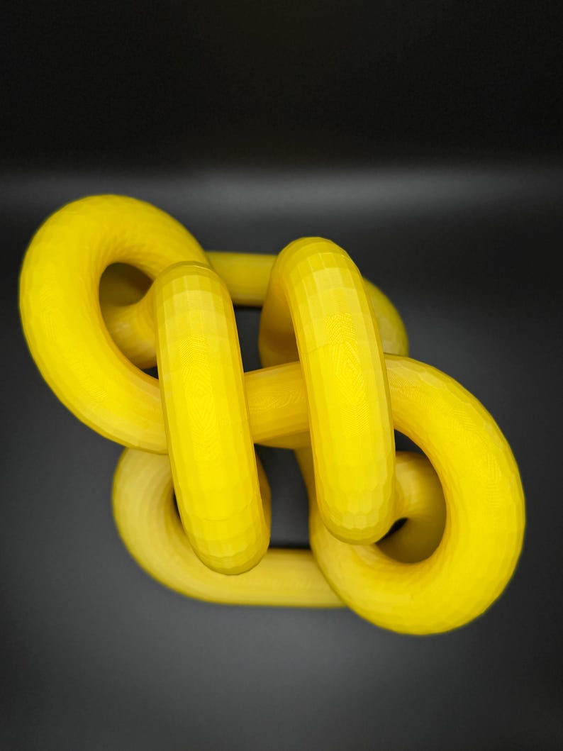 May include: A yellow plastic sculpture of a knot, with a smooth, glossy finish.