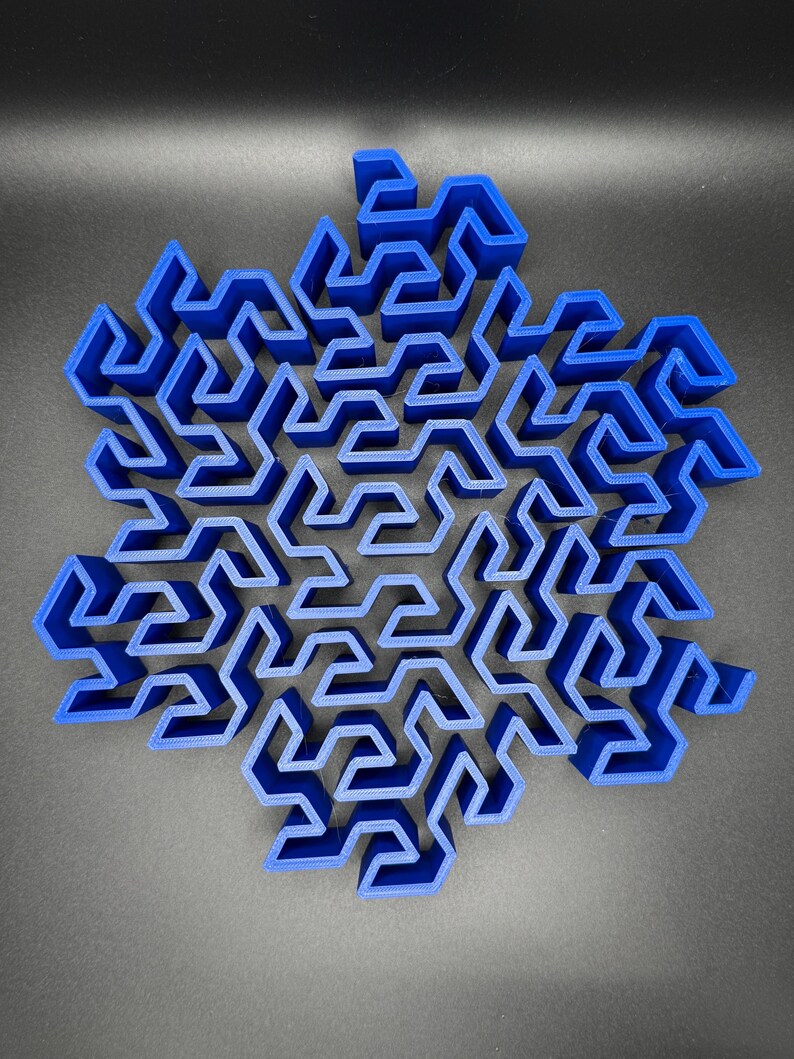 May include: A blue 3D printed snowflake shaped maze. The maze is made up of many small, intricate paths that wind and turn.
