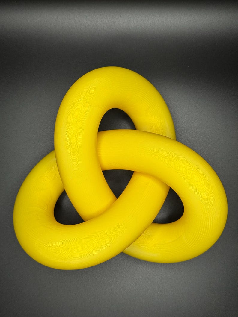 May include: A bright yellow, three-dimensional knot sculpture. The knot is made of three intertwined loops, each with a circular shape.