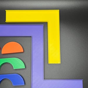 May include: Two L-shaped pieces of plastic, one yellow and one purple, are stacked on top of each other. Three semi-circular pieces of plastic, one orange, one green, and one blue, are arranged below the L-shaped pieces.